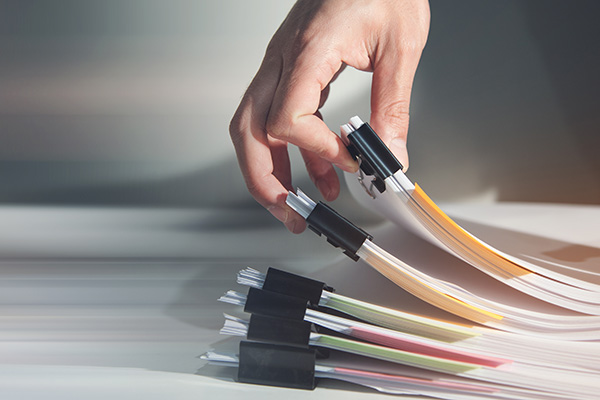 A hand picking up a stack of color-coded paper folders held together with black binder clips from a desk.